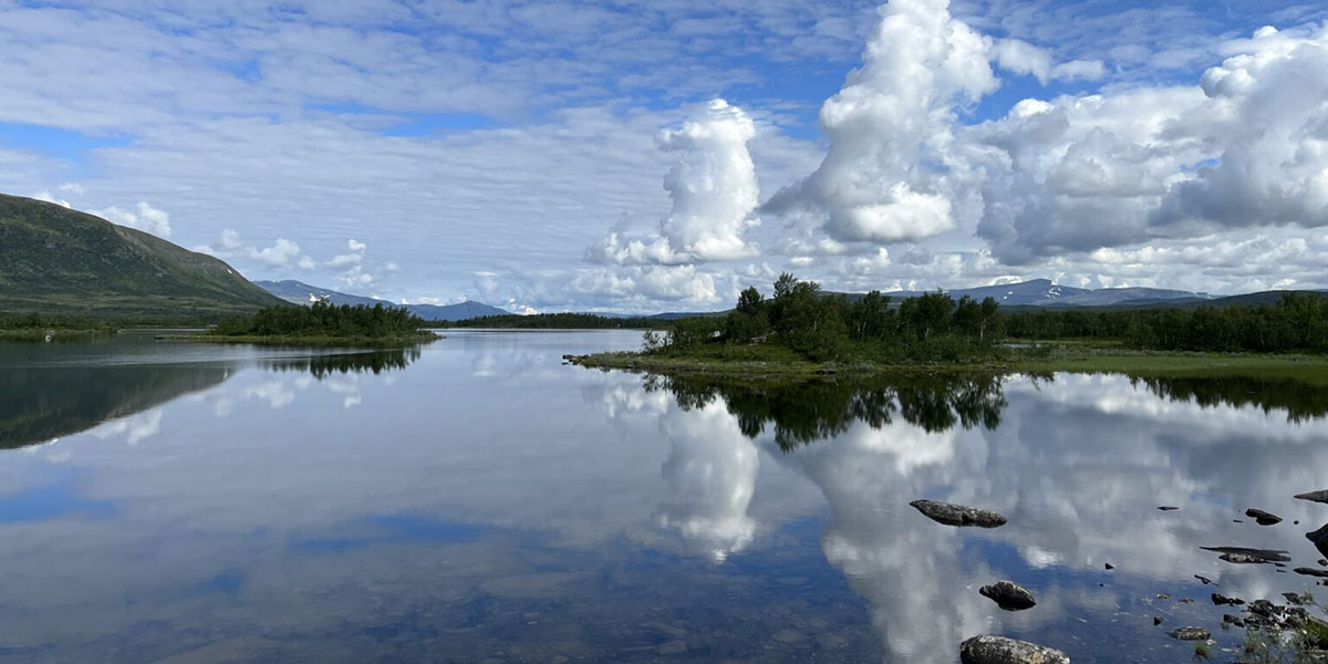 A crystal-clear lake with a forest and a few high hills in the background.